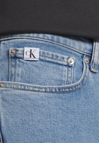 Ljusblå denimjeans med en liten vit etikett som har "cK." Inkluderar silverfärgade metallnaglar och en klassisk fickdesign.