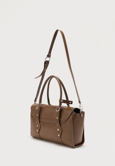 Καφέ δερμάτινη γυναικεία τσάντα με διπλές λαβές και ρυθμιζόμενο ιμάντα ώμου, επάνω σε απλό φωτεινό φόντο.