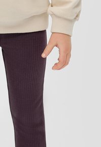 Beige sweatshirt met geribde manchetten, gecombineerd met donkergroene geribde legging, waarbij een kinderhand dicht bij de naad van de legging rust.
