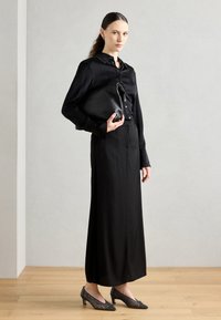 Črna svila s kragnico, dolga črna krila, teksturirane črne petke, drži črno usnjeno torbico. Enostavna, elegantna zasnova, gladka tekstura.