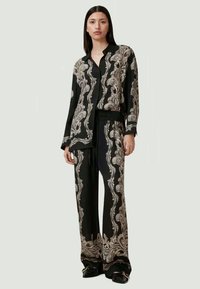 Svart mønstret sett som inkluderer en krage og knappet skjorte samt løse bukser, prydet med intrikate hvite paisleymønstre. Glatt tekstur.