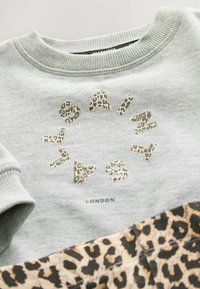 Ljusgrå sweatshirt med leopardmönstrad text och detaljer. Ribbad rundad halsringning och cuffar. Tyget har en mjuk och avslappnad känsla.