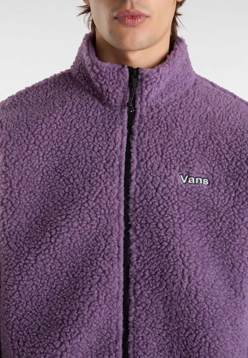 Lila Fleecejacke mit hohem Kragen, Reißverschluss und schwarzem Zipper. Verfügt über ein gesticktes "Vans"-Logo auf der linken Brust. Strukturierte Oberfläche.