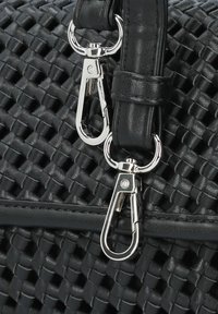 Bolso de mano tejido en negro con una superficie texturizada, correa de cuero suave y clips de hardware plateado para sujeción.