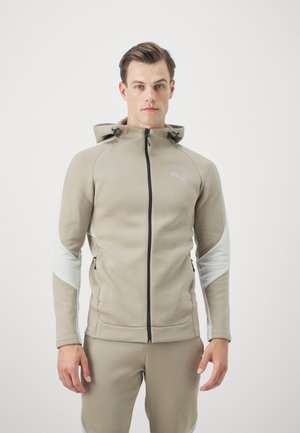 Giacca beige con cappuccio e dettagli grigi, con zip frontale, tasche laterali e logo Puma. Realizzata in tessuto morbido e testurizzato per il comfort.