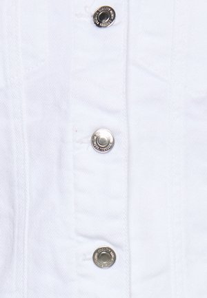 Närbild av vitt denimtyg med tre silverfärgade tryckknappar i en vertikal rad, sömmen synlig runt varje knapp.