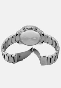 Zegarek ze stali nierdzewnej z metalową bransoletą, okrągłą kopertą i polerowanym wykończeniem. Posiada podwójny zamek na przycisk oraz przyciski chronografu.