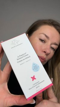 Woman holding a box of Drunk Elephant A-Passioni Retinol Cream with product details visible against a neutral background.