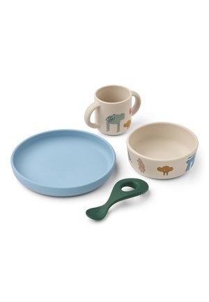 Juego de vajilla infantil con plato azul, bol beige y taza con dos asas con estampados de animales, y un mordedor con forma de cuchara verde.