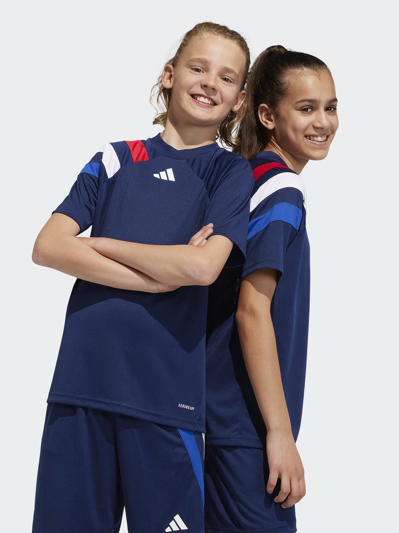 Dos niños llevan camisetas deportivas de color azul marino con acentos rojos y blancos en los hombros. La tela es suave y ligera, adecuada para el deporte.