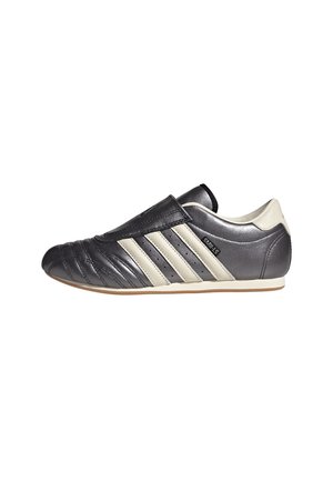 Schwarz-weißer Ledersneaker mit drei weißen Streifen an der Seite und einer flachen, niedrigen Sohle, von der Außenseite betrachtet.