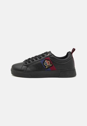 Black sneaker with textured synthetic upper, flat laces, side panel featuring red and blue accents, and embroidered logo detail. Rubber sole.