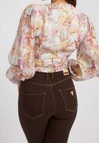 Blouse à motif floral avec manches bouffantes et tissu léger et transparent. Jean marron foncé avec surpiqûres contrastées et deux poches arrière.