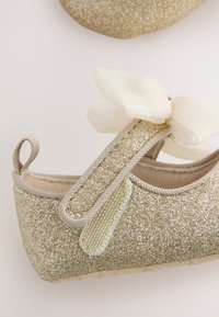 Kuldne sädelev baleriiniking bežika rihma ja pehme elevandiluu värvi paelaga. Tekstureeritud pealiskihiga, sile sisevooder, kannal aas kergemaks jalga panekuks.