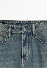 Jeans in denim blu chiaro con un classico design a cinque tasche, chiusura con bottone e dettagli leggermente usurati lungo il tessuto.