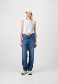 Bílý žebrovaný crop top spárovaný s modrými volnými džíny a světlými teniskami. Bílá baseballová čepice dotváří celý outfit.