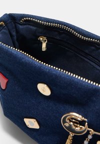 Intérieur d'un sac à main en denim avec une fermeture éclair dorée, plusieurs boutons décoratifs et une petite poche zippée, de couleur bleu foncé et texture lisse.