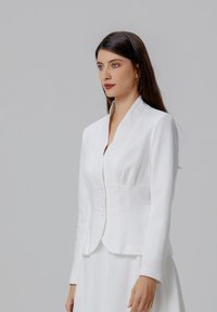 Blazer blanc avec une coupe ajustée, un col cranté et une fermeture à bouton. Tissu lisse avec des manches longues et des détails de couture subtils.