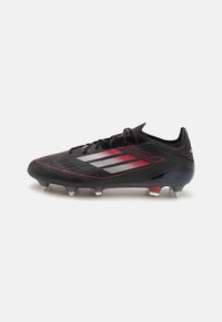 Black football cleats with a textured design, featuring red and silver accents, a low profile silhouette, and six conical studs on the outsole.