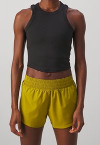 Czarny krótki top na ramiączkach wykonany z gładkiej tkaniny, zestawiony z krótkimi spodenkami o długości do kolan w jasnym oliwkowym zielonym kolorze z elastyczną talią. Prosty krój, bez wzorów.