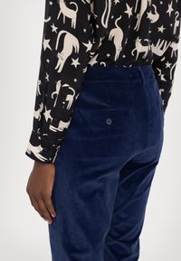 Chemise noire avec imprimé de chat crème et étoiles, manches longues, poignets à boutons ; pantalon en velours côtelé marine avec poche arrière et détail bouton.