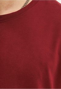 Bordeaux bomulds t-shirt med rund hals og fin tekstur. Har diskrete syninger og en glat stoffoverflade.