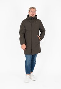 Giacca a pallone marrone con cappuccio, zip frontale e tasche laterali. Indossata su jeans blu e sneakers bianche, con un design pulito e semplice.