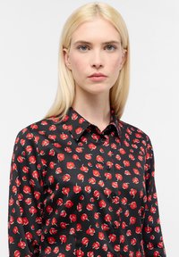 Sort button-up skjorte med en blank overflade, prydet med et rødt blomstermønster og en klassisk kravedesign.