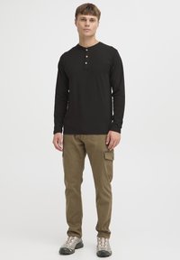 Zwart langarm henley-shirt met houten knoppen, gecombineerd met khaki cargobroek met zijzakken en een geribbelde textuur.