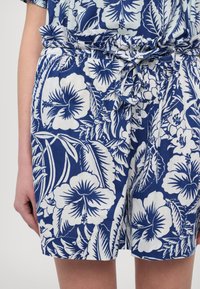 Blå og hvite shorts med blomstermønster laget av lett stoff, med elastisk linning og en knyttet sløyfedetalj.