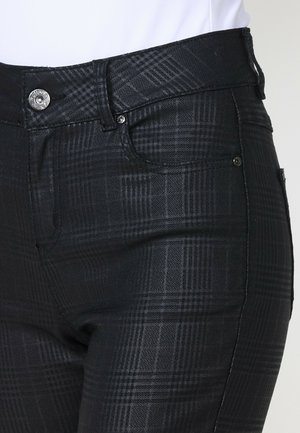 Jean à carreaux noir avec une texture lisse, taille mi-haute, poches avant et éléments en métal. Le motif à carreaux ajoute de l'intérêt visuel.
