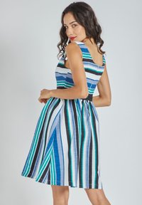 Vestido a rayas en azul, blanco y negro. Presenta un corsé ajustado, falda acampanada y tirantes anchos. Tejido texturizado con líneas verticales.