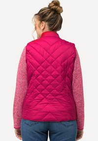 Rosa gesteppte Weste mit hohem Kragen und Rautenmuster, kombiniert mit einem strukturierten rosa Langarmshirt. Die Rückansicht zeigt kontrastierende Farben.