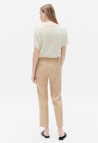 Top in maglia beige con scollatura ampia abbinato a pantaloni tailored marrone chiaro con due tasche posteriori, texture liscia e gambe affusolate.