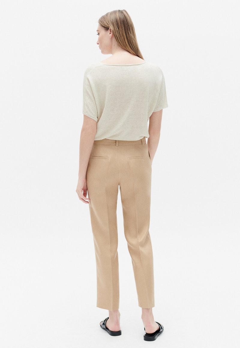 Beige gebreide top met een brede halslijn, gecombineerd met lichtbruine tailored broeken met twee achterzakken, een gladde textuur en taps toelopende benen.