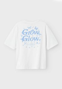 Biała bawełniana koszulka z niebieskim wzorem graficznym, na którym znajduje się napis "Grow Glow" otoczony motylami i elementami florystycznymi.