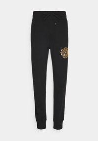 Schwarze Jogginghosen aus Baumwolle mit Kordelzugbund. Mit einem goldenen, dekorativen Logo am linken Oberschenkel. An den Knöcheln mit Bündchen versehen.