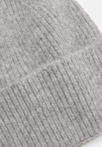 Grå stickad mössa i mjuk ull, med ribbad textur och växlande upphöjda och platta mönster. Dekorativa inslag inkluderar en vikbar kant.