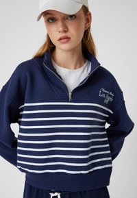 Granatowy sweter z białymi poziomymi paskami, zamek błyskawiczny do ćwierć długości z przodu i haftowanym detalem "Los Angeles 1998". Miękka tkanina z mieszanki bawełny.