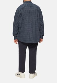 Marineblauw geruit shirt met lange mouwen, relaxed fit en een button-down kraag, gecombineerd met marineblauwe broek en witte sneakers.