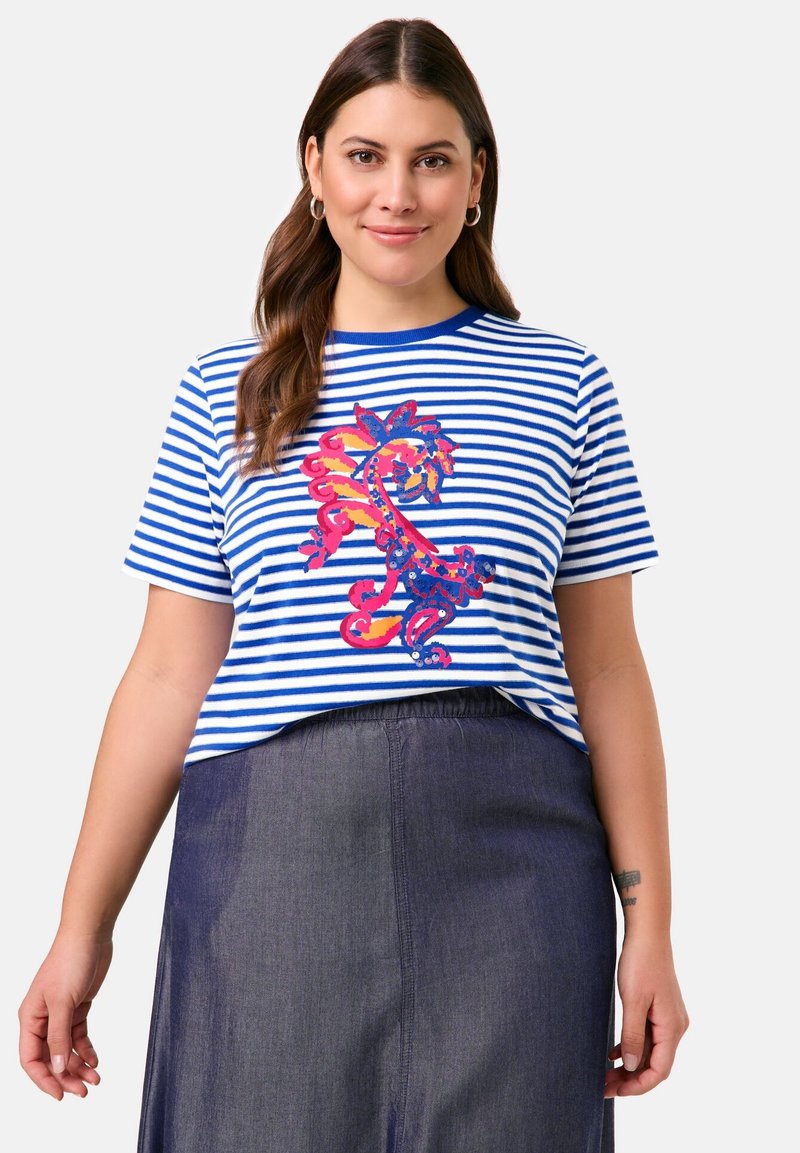 Blau-weiß gestreastes Kurzarm-T-Shirt mit buntem Dracheneinstick. Weicher Stoff, lässiger Schnitt, Rundhalsausschnitt. Getragen mit einem dunklen Rock.