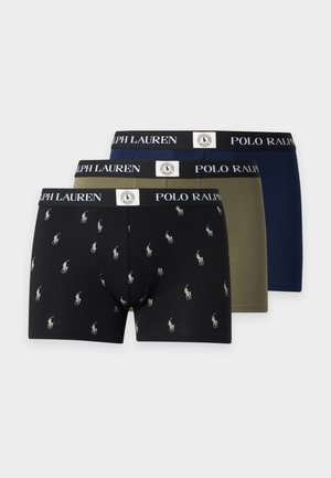 Jeune homme à la carrure musclée portant un boxer vert olive avec une ceinture noire Polo Ralph Lauren, debout pieds nus sur fond blanc.