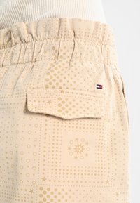 Pantalones cortos beige con cintura elástica, que presentan una variedad de patrones en relieve, incluyendo círculos y estrellas. Incluye un detalle de bolsillo lateral.