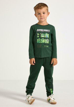 Maglietta verde a maniche lunghe con grafica di Minecraft e pantaloni del pigiama verdi. Tessuto morbido, vestibilità comoda e dettagli delle scarpe in contrasto.