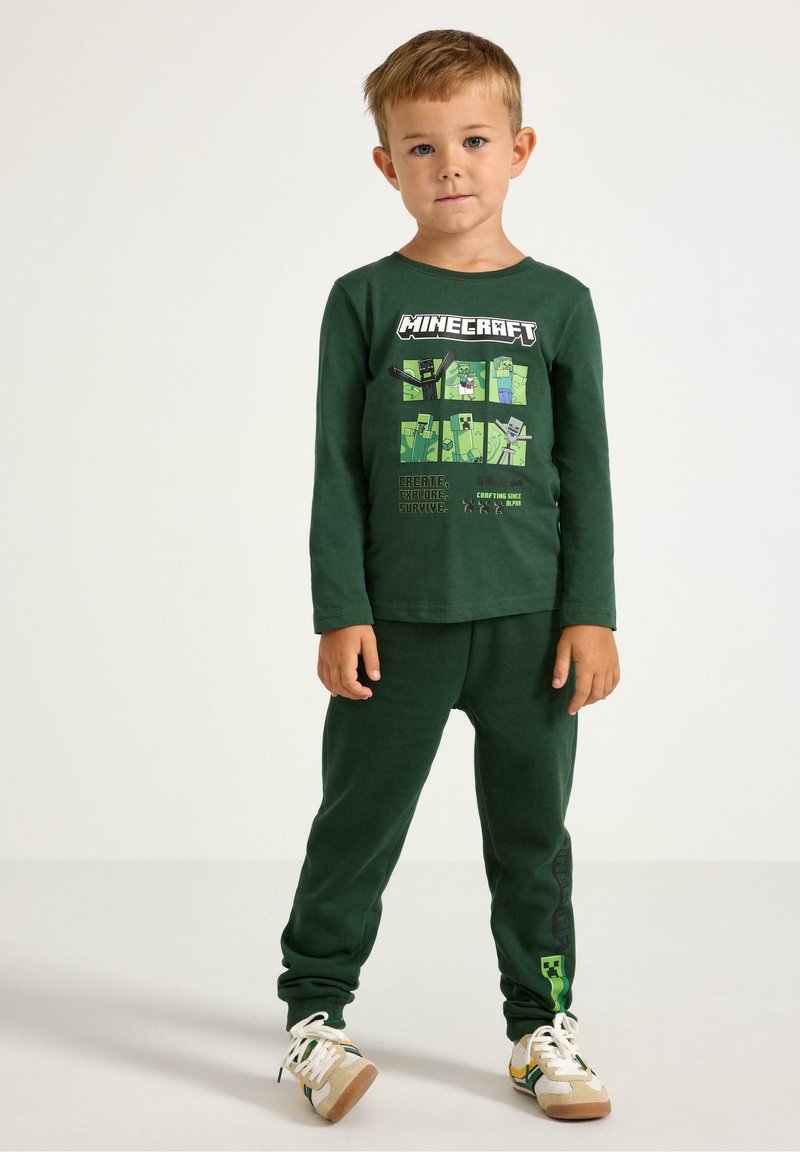 Maglietta verde a maniche lunghe con grafica di Minecraft e pantaloni del pigiama verdi. Tessuto morbido, vestibilità comoda e dettagli delle scarpe in contrasto.