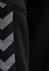 Primo piano di tessuto nero a coste con un pannello con strisce bianche a chevron in un motivo verticale.