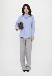 Camicia a righe blu e bianche con un design di rosa sul colletto, pantaloni grigi a gamba larga e una piccola borsa marrone, abbinati a scarpe nere a punta.