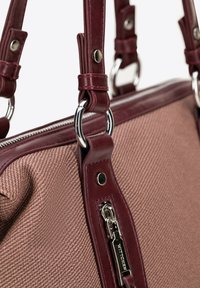 Torba na ramię z teksturowanej różowej tkaniny, z głębokimi burgundowymi skórzanymi akcentami i paskami. Wyposażona w srebrne okucia i zamek błyskawiczny.