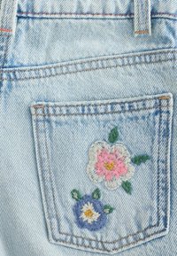 Light blue denim pocket with embroidered pink and blue flowers and green leaves on the back of jeans with visible orange stitching.