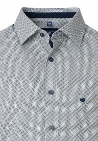 Geprinte blouse met knopen in lichtcrème met een herhalend blauw en marine patroon. Voorzien van een gestructureerde kraag en marine knopen.